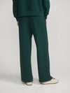 A person shown from the back wearing dark green wide-leg trousers and a matching dark green top, paired with off-white sneakers, against a light gray studio background.