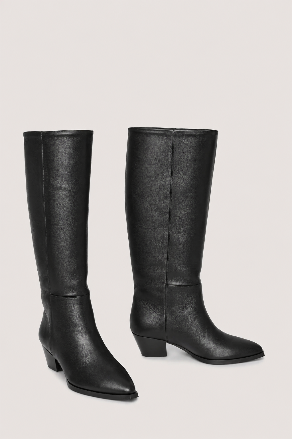 A pair of black leather knee-high boots with low block heels and pointed toes, displayed against a solid light gray background.