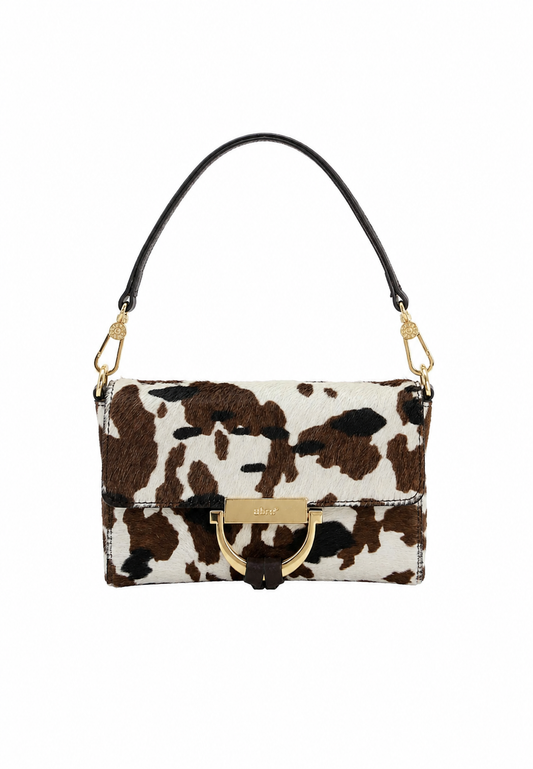 A small wristlet clutch with a brown and white cow print pattern, a dark brown wrist strap, and gold-tone hardware, shown against a plain white background.