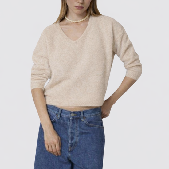Woman wearing a beige sweater and blue jeans on a white background