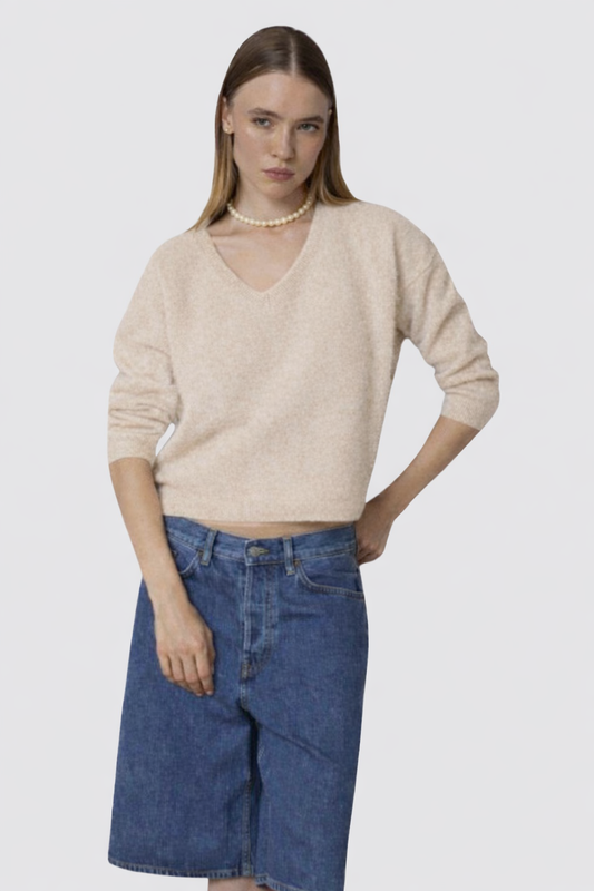 Woman wearing a beige sweater and blue jeans on a white background