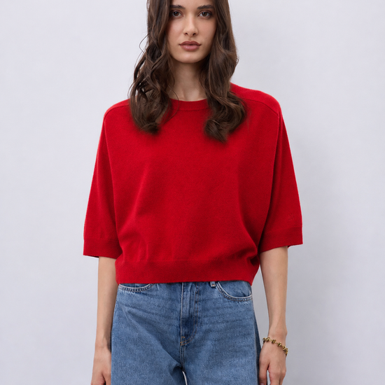 Model wearing a bright red cashmere mid length sleeve knit, with blue jeans on a white background
