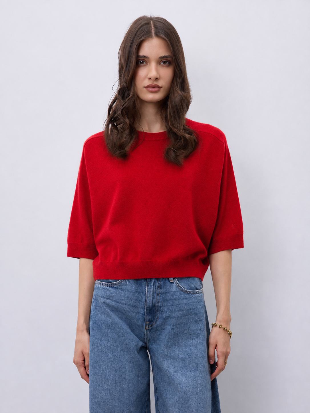 Model wearing a bright red cashmere mid length sleeve knit, with blue jeans on a white background