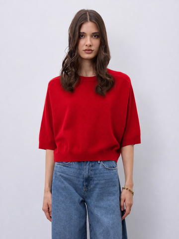 Model wearing a bright red cashmere mid length sleeve knit, with blue jeans on a white background