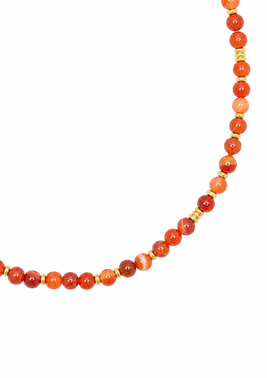 A beaded necklace featuring round orange and red agate beads separated by small gold spacer beads, shown against a plain white background.