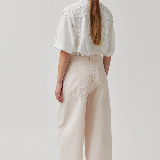 Person wearing a white lace top and beige pants on a plain background