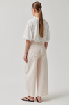 Person wearing a white lace top and beige pants on a plain background