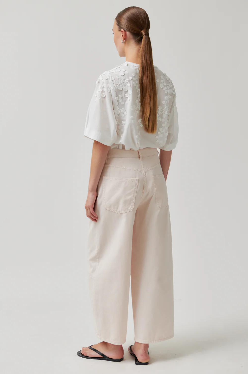 Person wearing a white lace top and beige pants on a plain background