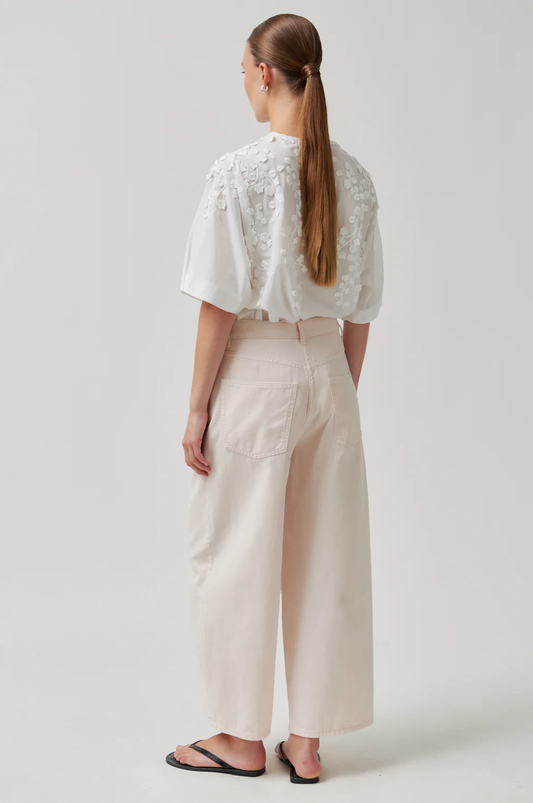 Person wearing a white lace top and beige pants on a plain background