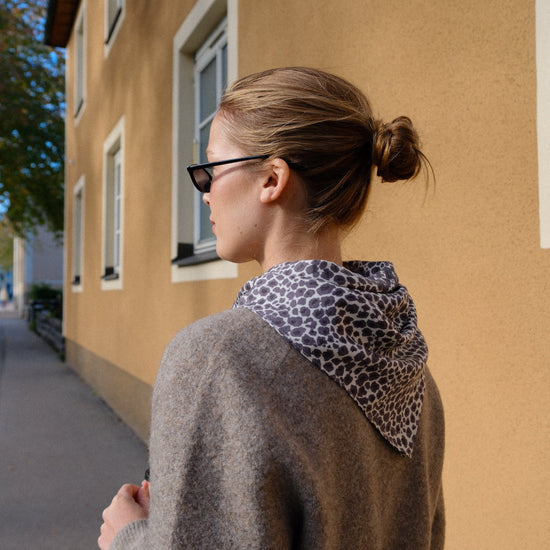 Woman wearing a leopard print scarf and sunglasses, standing on a street.