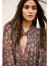 A woman wearing a bohemian-style long-sleeve blouse with a deep V-neckline and tie-neck detail, featuring a rust red, beige, and blue paisley pattern.