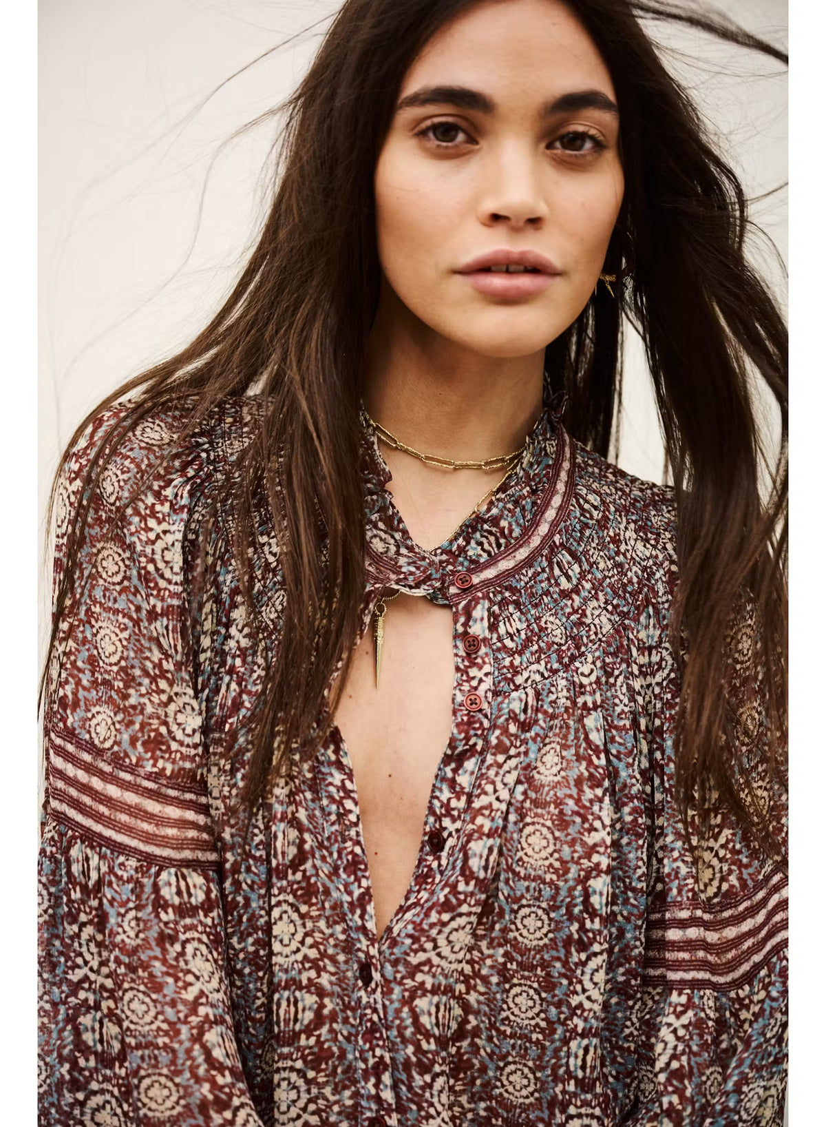 A woman wearing a bohemian-style long-sleeve blouse with a deep V-neckline and tie-neck detail, featuring a rust red, beige, and blue paisley pattern.