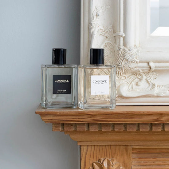 Two Connock perfume bottles on a wooden surface with a decorative mirror in the background.
