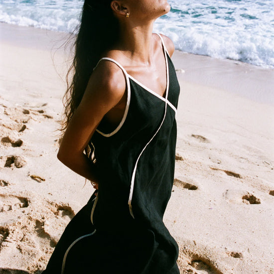 Woman in a black dress with white trim on a beach from Lilly Pilly