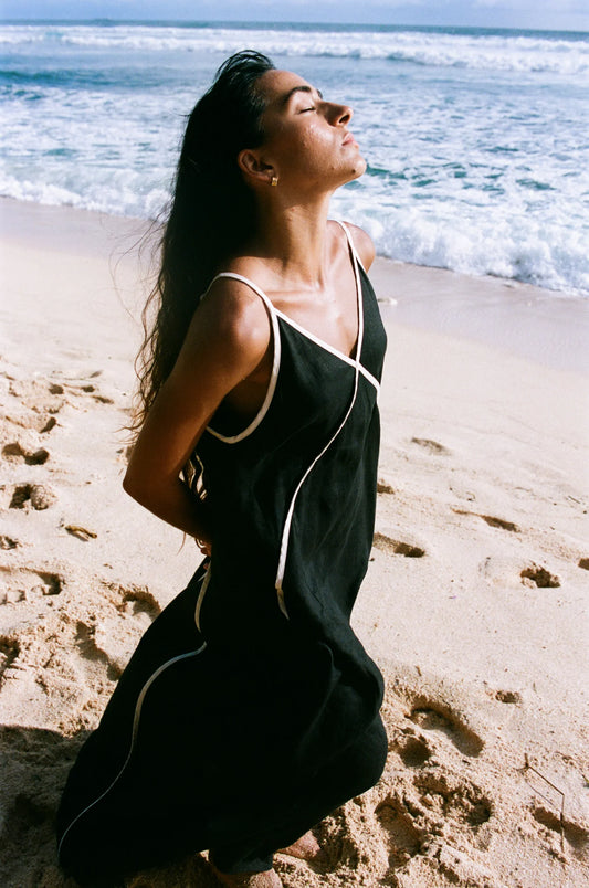 Woman in a black dress with white trim on a beach from Lilly Pilly