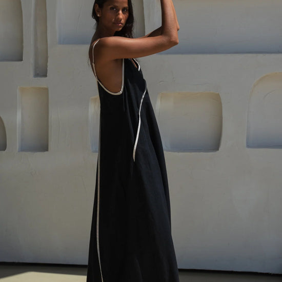 Woman in a black dress with white trim standing against a light-colored wall.