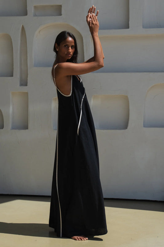 Woman in a black dress with white trim standing against a light-colored wall.