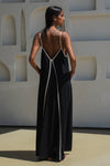Reverse of Woman wearing a black dress with white straps against a light-coloured wall.
