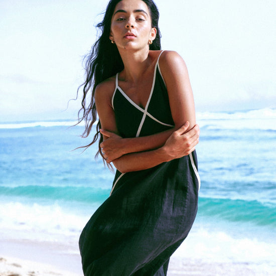 Woman in a black dress standing on a beach with ocean and sky in the background