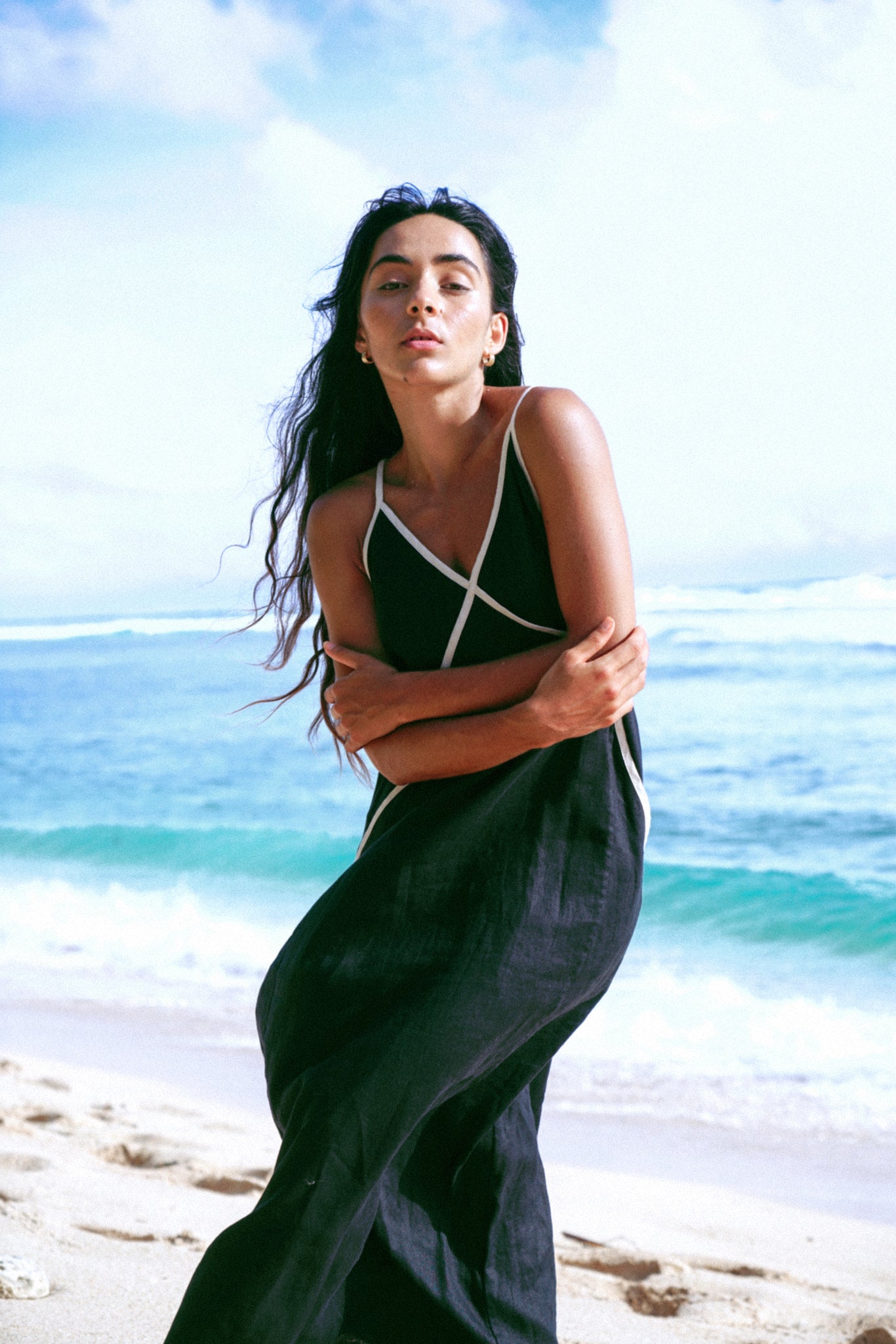 Woman in a black dress standing on a beach with ocean and sky in the background
