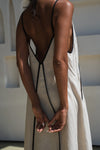 Person wearing a beige linen dress with thin straps in an abstract indoor setting