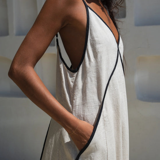 Woman wearing a beige linen dress with black trim in a minimal indoor setting