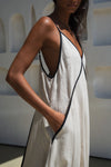Woman wearing a beige linen dress with black trim in a minimal indoor setting