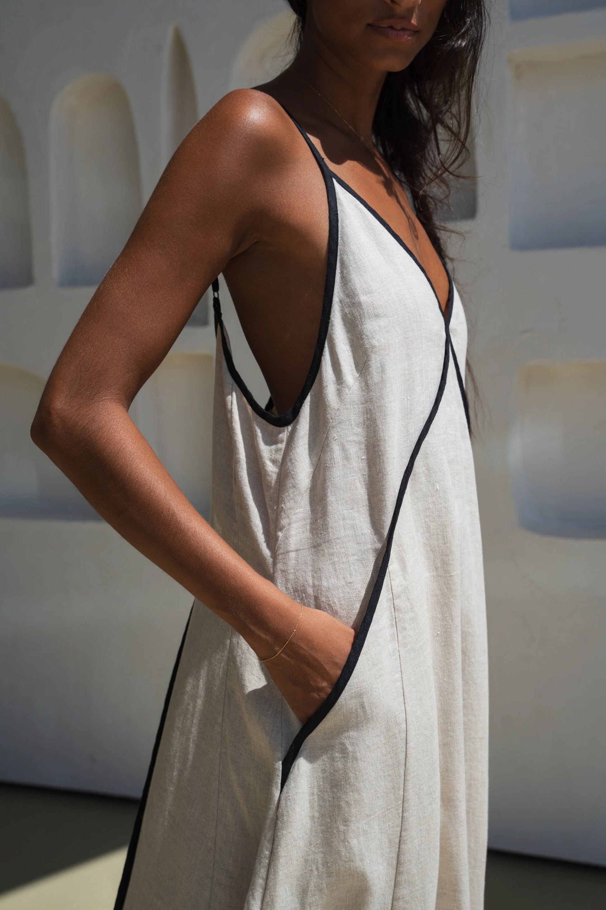 Woman wearing a beige linen dress with black trim in a minimal indoor setting