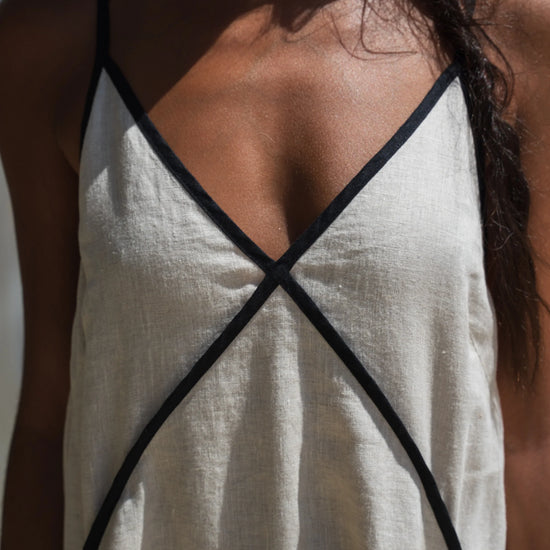 top of beige linen dress with black straps worn by a person against a neutral background