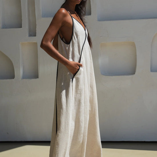 Woman in a white linen dress standing against a light-colored wall with geometric patterns.