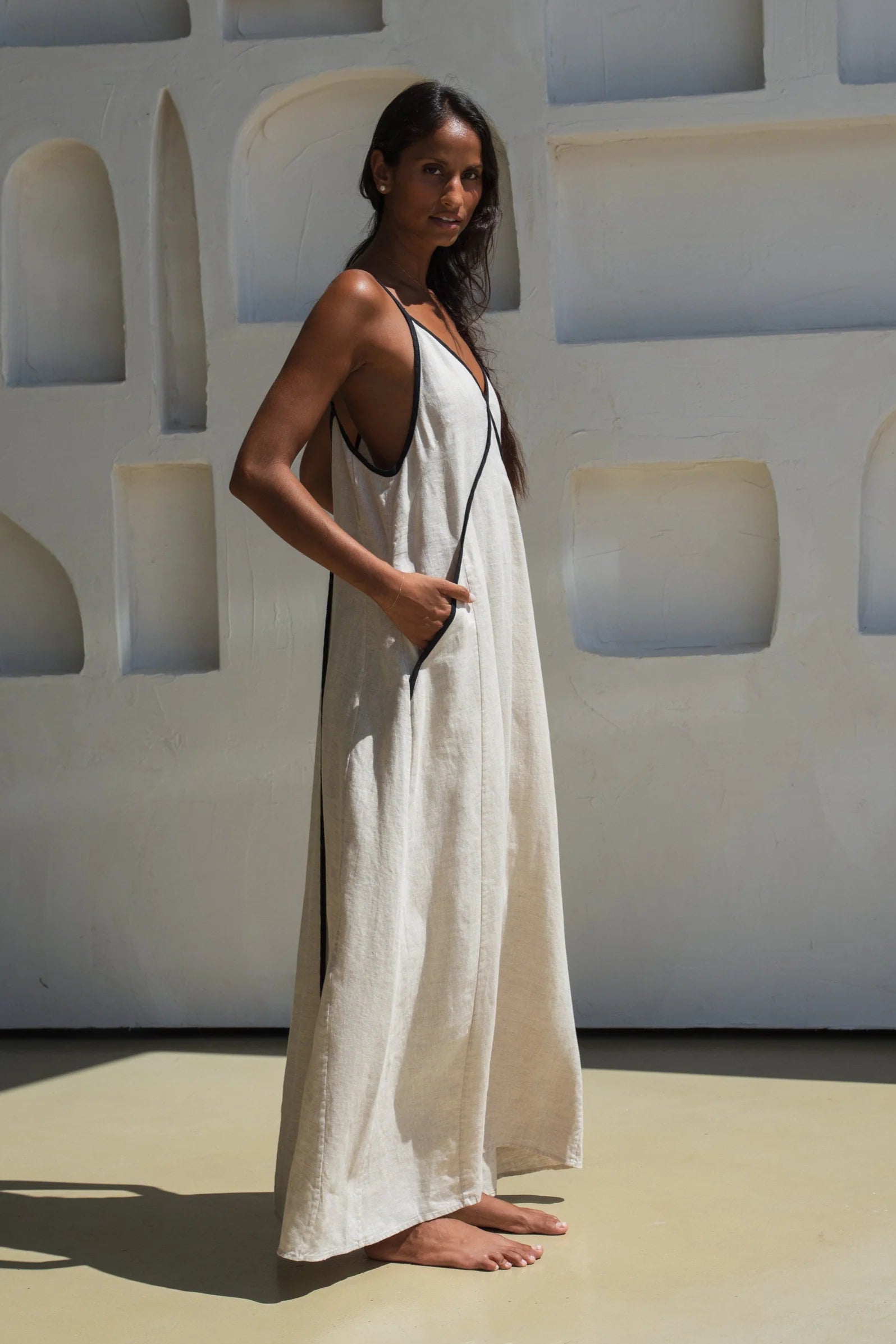 Woman in a white linen dress standing against a light-colored wall with geometric patterns.
