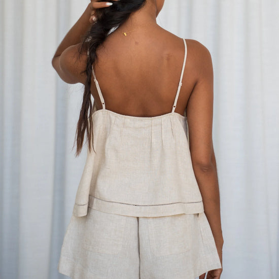 Woman wearing a beige linen top and shorts set against a white curtain background