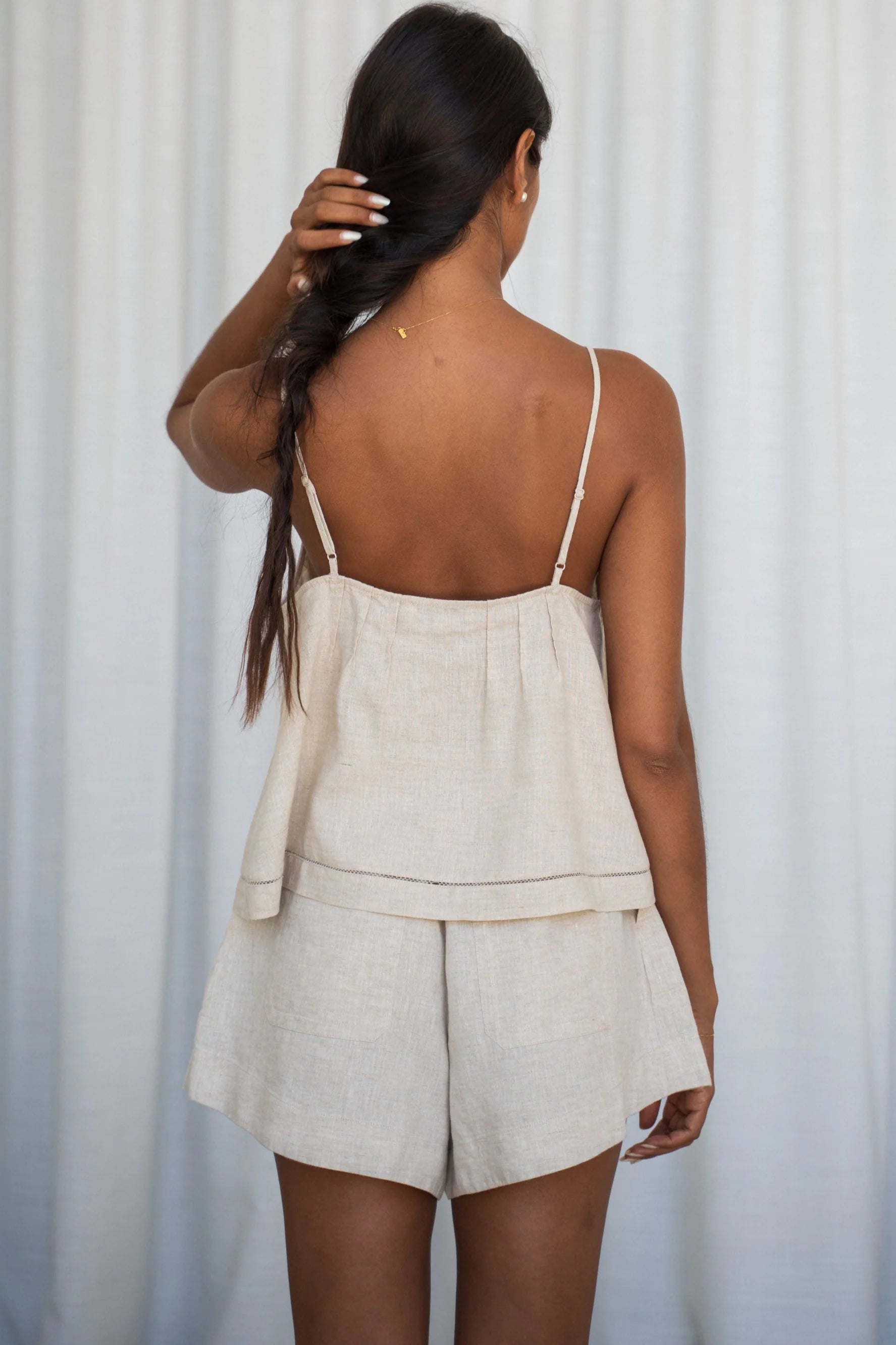 Woman wearing a beige linen top and shorts set against a white curtain background
