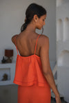 Woman wearing an orange linen top with a blurred indoor background