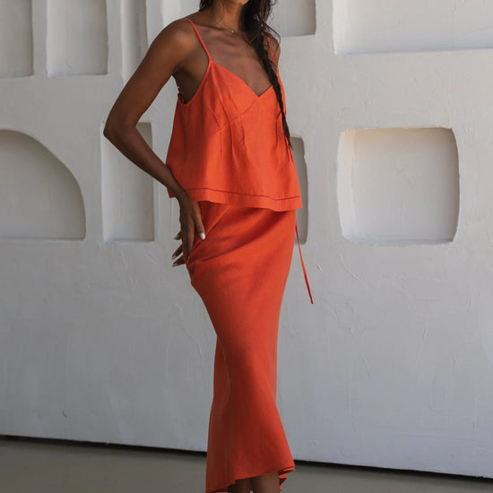 Woman wearing an orange linen co-ord standing against a white wall with geometric shapes.
