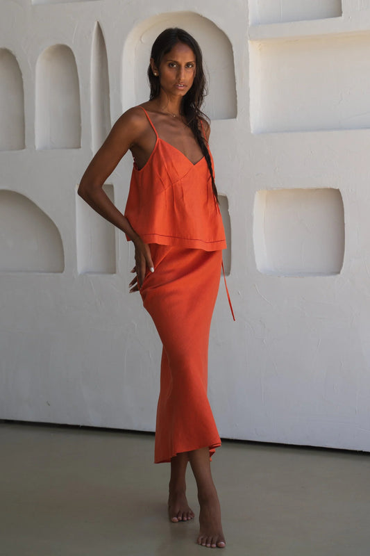 Woman wearing an orange linen co-ord standing against a white wall with geometric shapes.