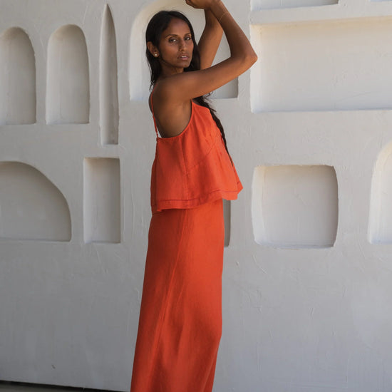 Woman in an orange linen top and skirt standing against a white textured wall.