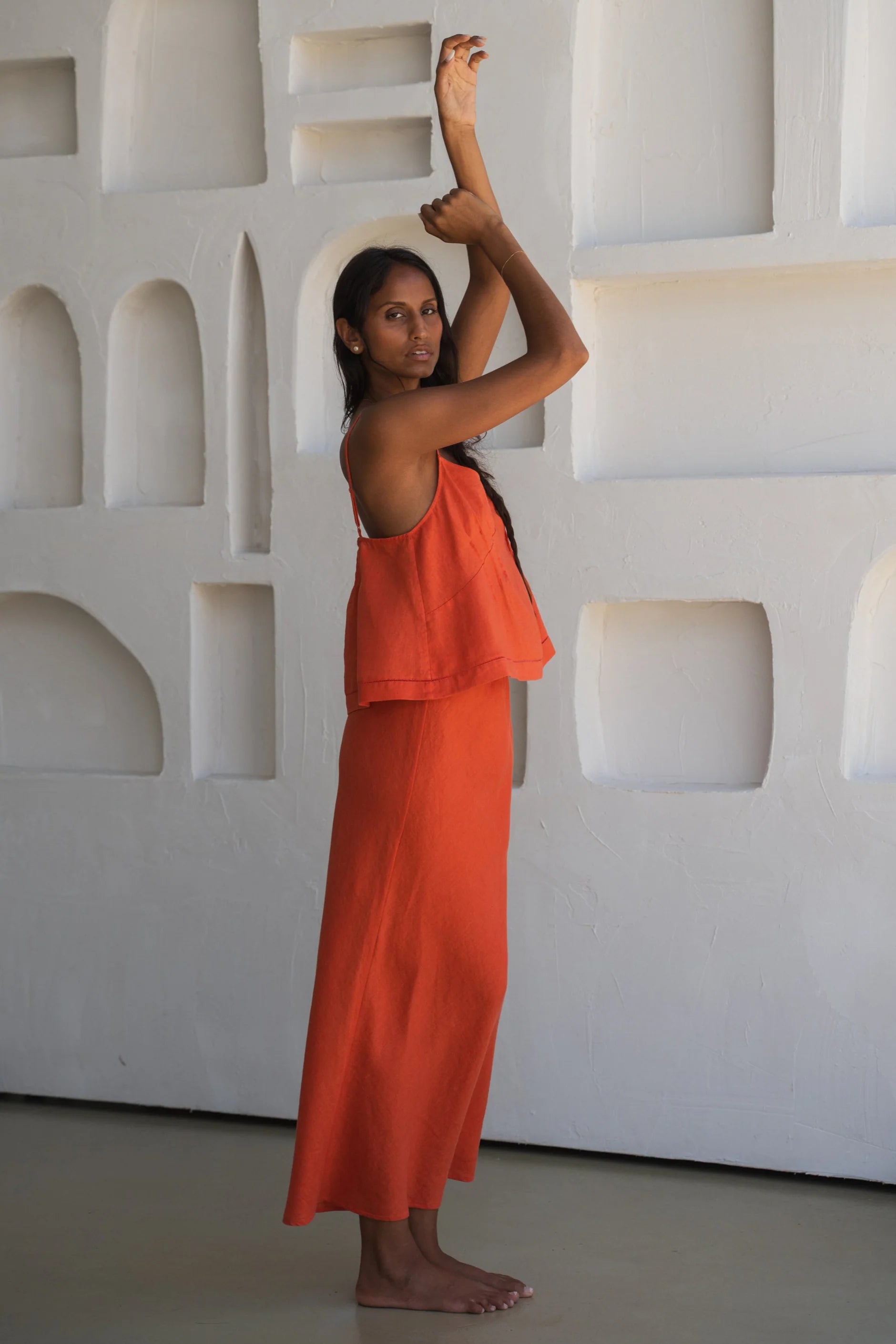 Woman in an orange linen top and skirt standing against a white textured wall.
