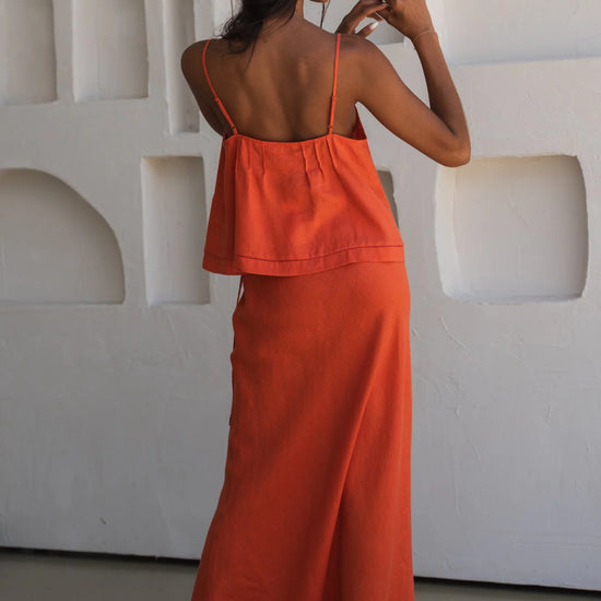 Woman wearing an orange linen outfit standing against a white textured wall.