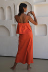 Woman wearing an orange linen outfit standing against a white textured wall.