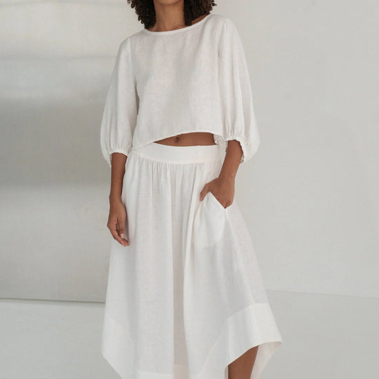 Woman wearing a white linen outfit against a plain background