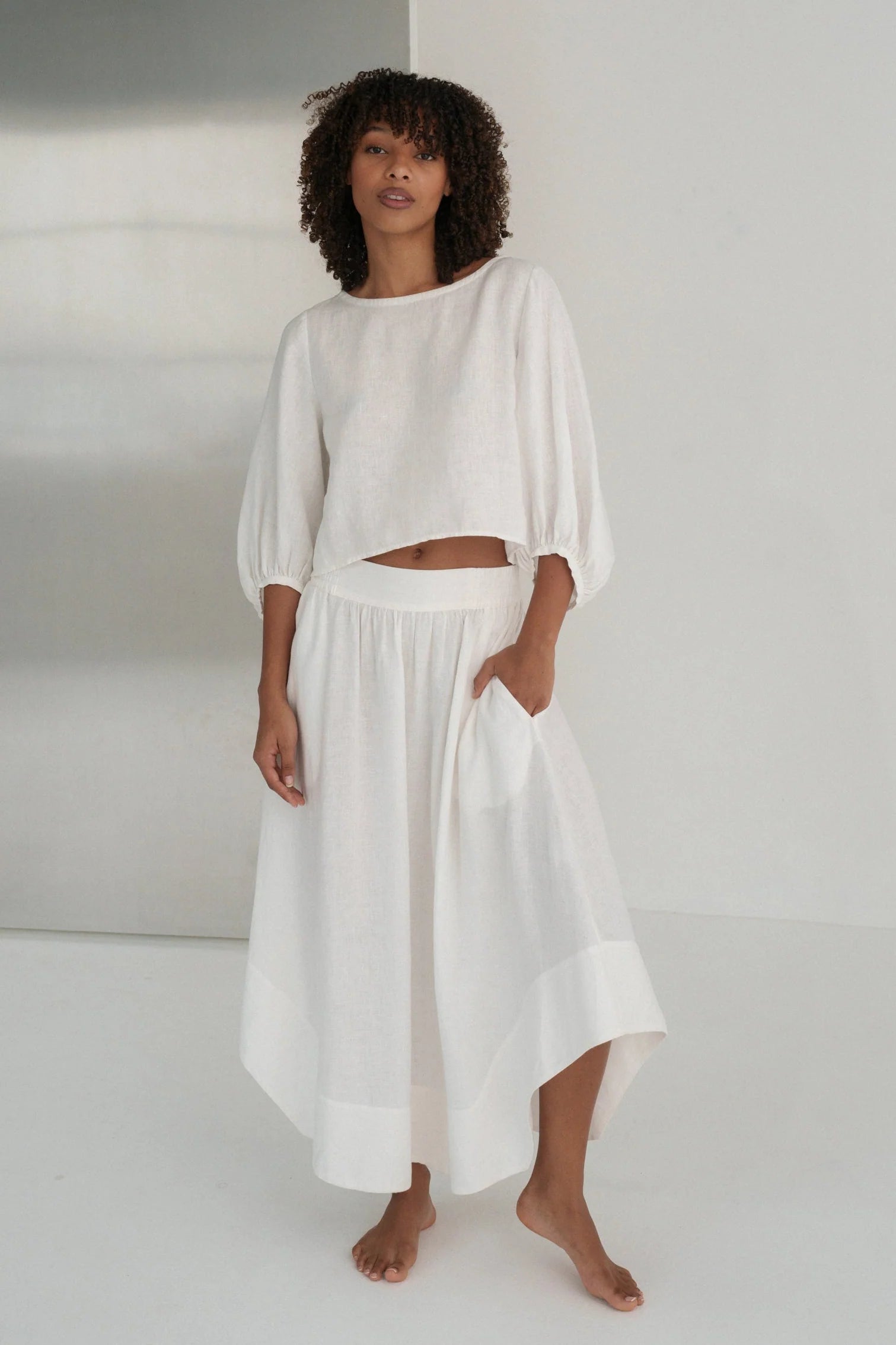 Woman wearing a white linen outfit against a plain background