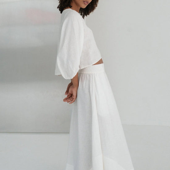 Woman wearing a white linen outfit against a plain background