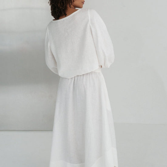 Person wearing a white linen top and skirt against a plain background