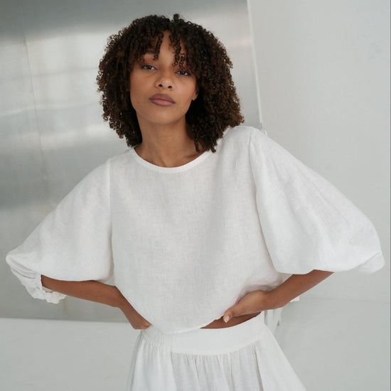 Woman wearing a white top  with puffed sleeves against a plain background