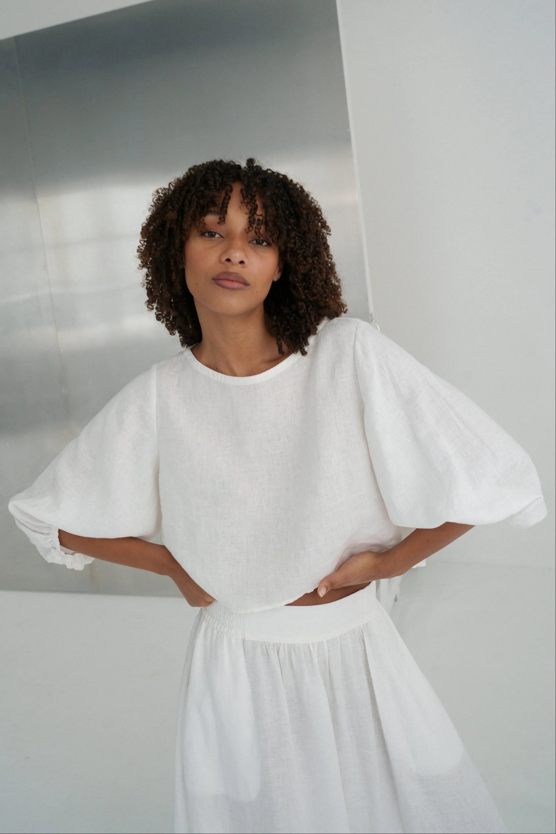 Woman wearing a white top  with puffed sleeves against a plain background