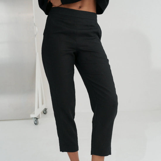 Person wearing black linen trousers and a black top against a white background