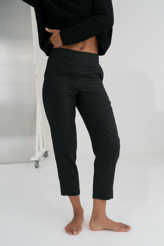 Person wearing black linen trousers and a black top against a white background