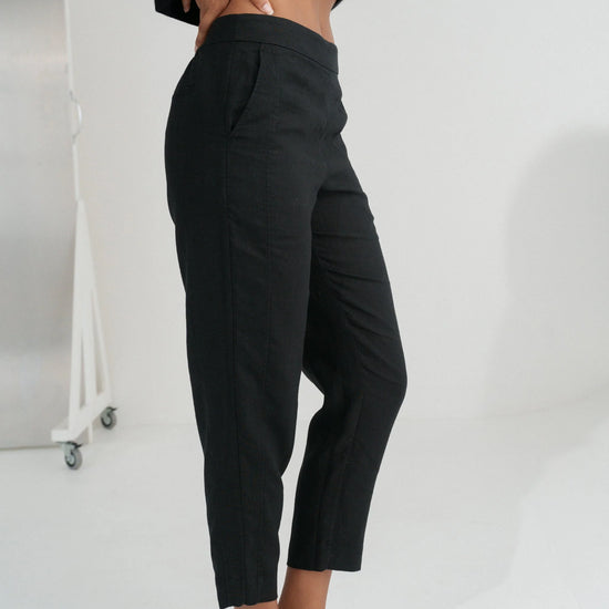 Person wearing black linen trousers on a plain white background