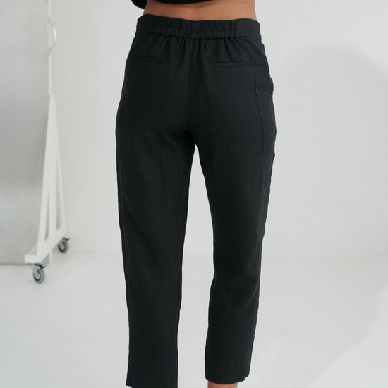 Person wearing black linen trousers against a white background